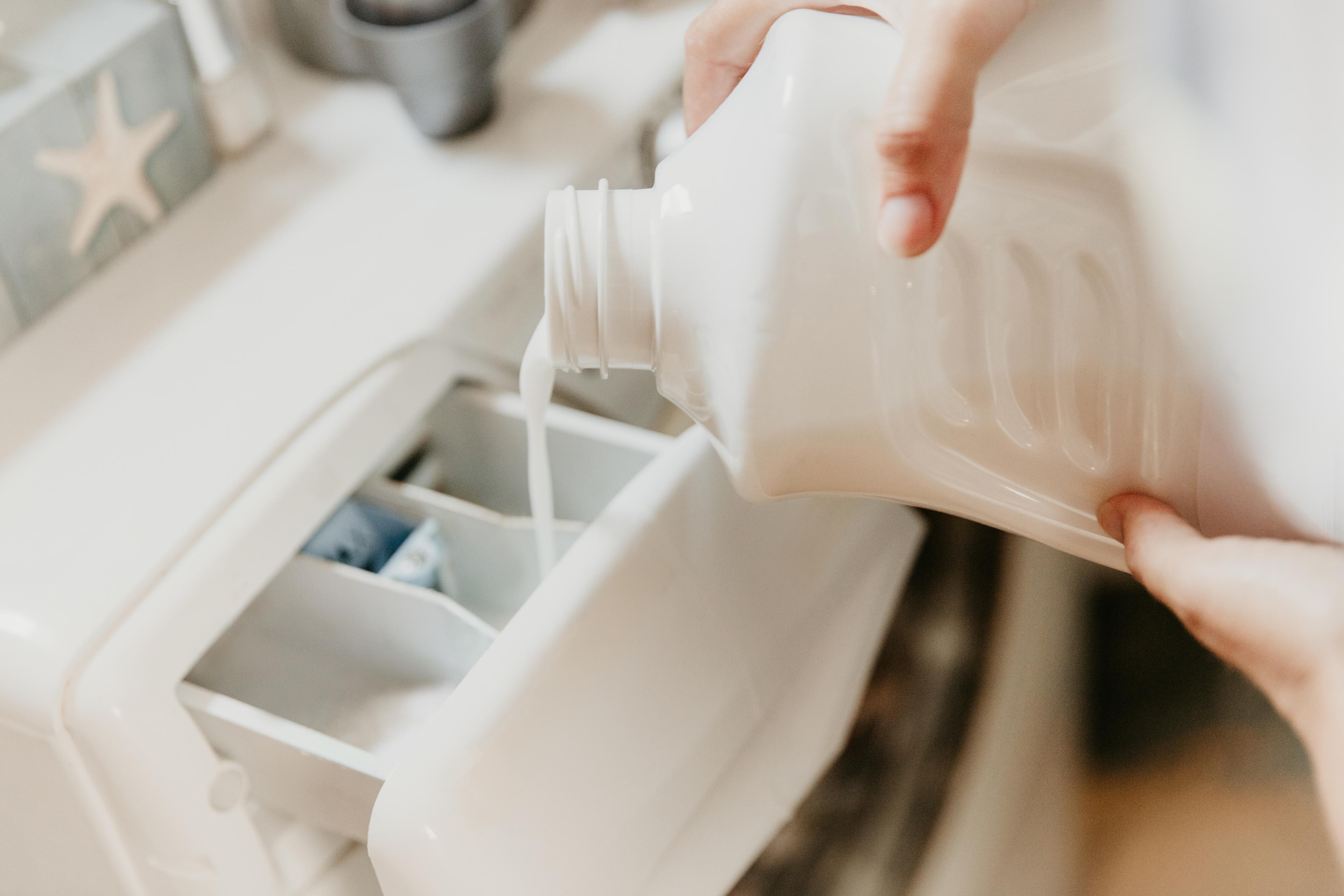 Woman pouring washing liquid detergent in washing machine at home